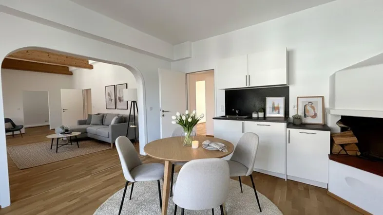 Heller offener Wohnbereich mit kleiner Küche, Essplatz und Kamin, verbunden mit einem weiteren Wohnzimmer.