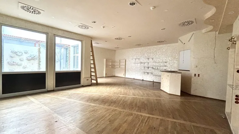 Geräumiger Ladenbereich mit Holzboden, großen Fenstern und Regalsystemen, bereit zur individuellen Gestaltung.