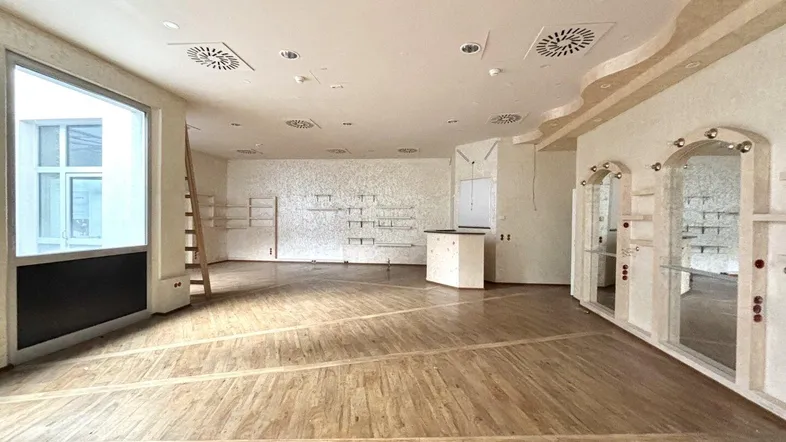 Geräumiger Ladenbereich mit Holzboden, großen Fenstern und dekorativen Wandelementen, bereit zur Einrichtung.