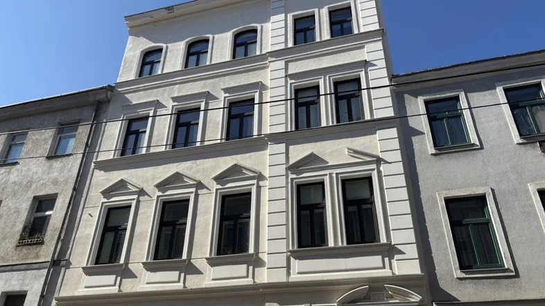 Vorderansicht eines klassischen Altbaus mit weißer Fassade und dunklen Fenstern.