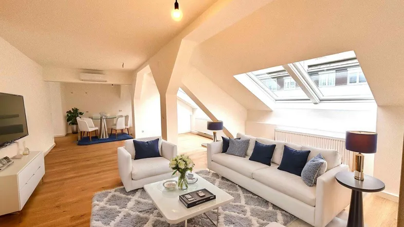 Helles Dachgeschoss-Wohnzimmer mit Holzboden, Dachfenstern und Essbereich im Hintergrund.