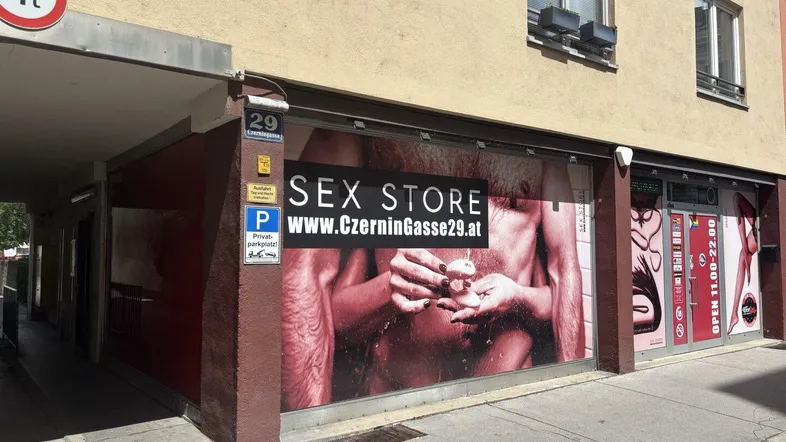 Gebäude mit Ladenlokal im Erdgeschoss und überdachtem Eingangsbereich an einer Straße.