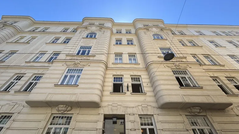 Eindrucksvolle Fassade eines Altbaus mit reich verzierten Details und großen Fenstern unter blauem Himmel.