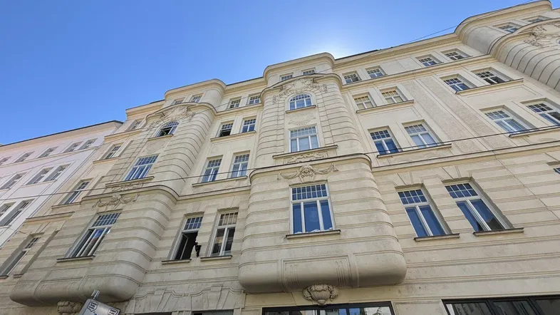 Historische Fassade eines Mehrfamilienhauses mit vielen Fenstern und architektonischen Details unter blauem Himmel.