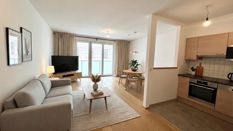Helles Wohn-Esszimmer mit Holzboden, Sofa, Esstisch und integrierter Küche.