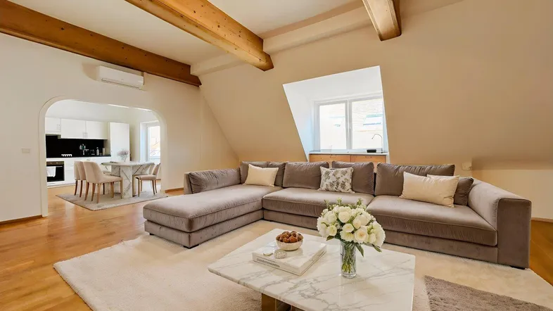 Geräumiger Wohn-Essbereich mit Holzbalken, gemütlichem Sofa und offenem Zugang zur Küche.