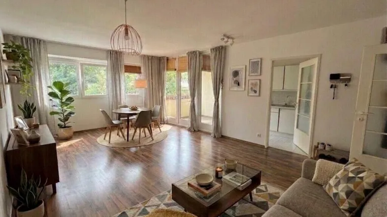 Helles Wohn- und Esszimmer mit Holzboden, modernen Möbeln und Zugang zum Balkon.