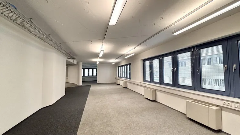 Großes, offenes Büro mit Teppichboden, vielen Fenstern und moderner Beleuchtung.