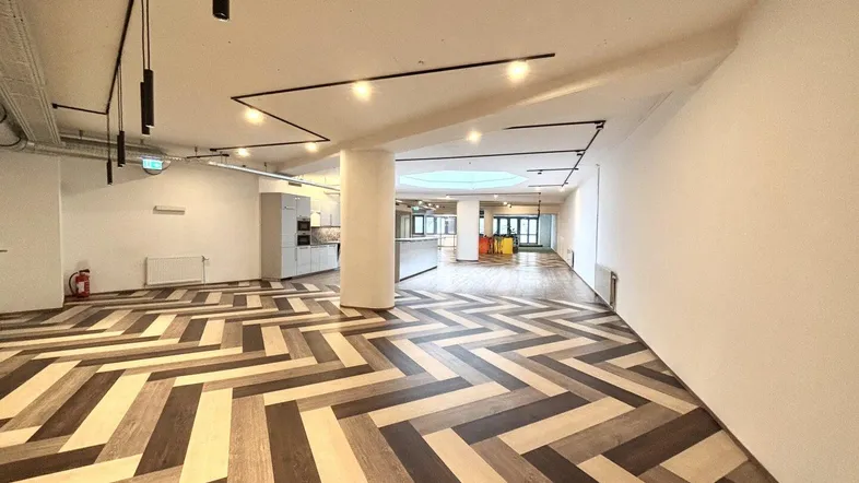 Geräumiger, offener Bürobereich mit modernem Fischgrät-Laminatboden und integrierter Küchenzeile.