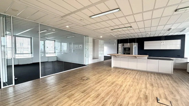 Geräumiges Büro mit moderner Küchenzeile, Holzboden und Glaswänden für separate Arbeitsbereiche.