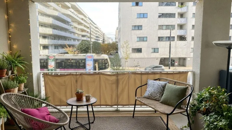 Möblierter Balkon mit Pflanzen und Blick auf die Stadtstraße und umliegende Gebäude.