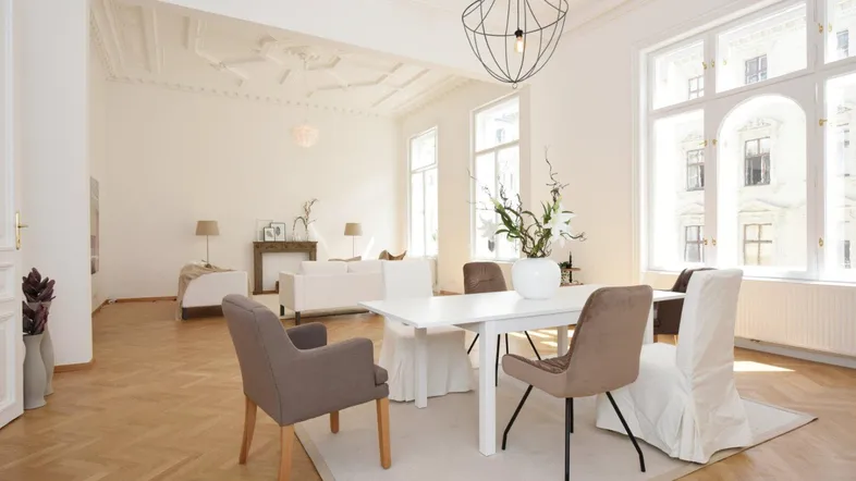 Helles Wohn- und Esszimmer mit Fischgrätparkett, Stuckdecke und großen Fenstern.