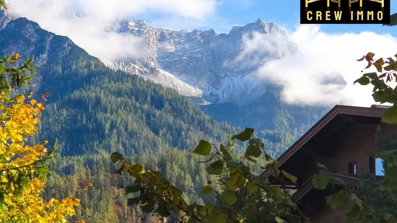 Malerische Berglandschaft mit schneebedeckten Gipfeln und einem traditionellen Haus im Vordergrund.