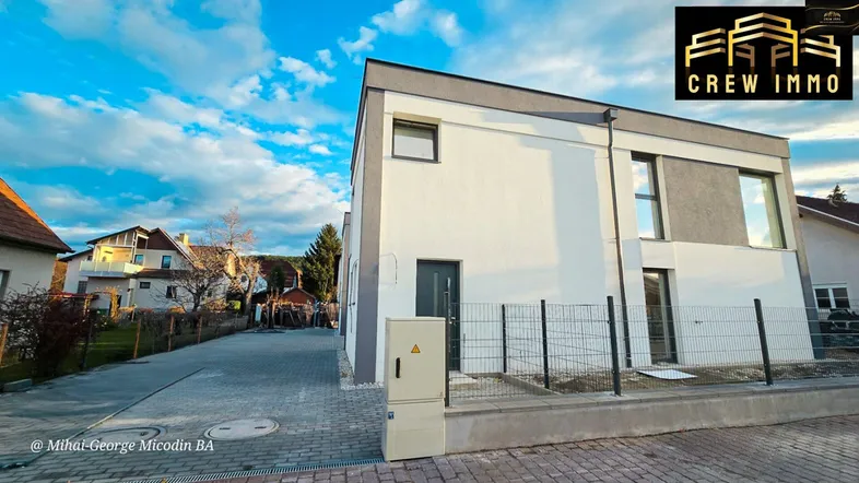 Modernes Einfamilienhaus mit weißer und grauer Fassade unter blauem Himmel und gepflasterter Zufahrt.