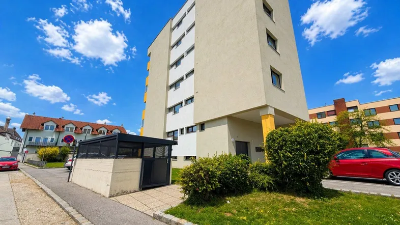 Mehrstöckiges Wohngebäude mit beiger Fassade und Parkplätzen im Freien unter blauem Himmel.