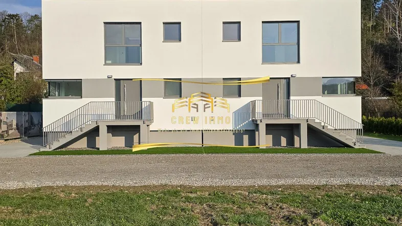 Moderne Doppelhaushälfte mit weißer Fassade und separaten Eingängen, umgeben von Natur.