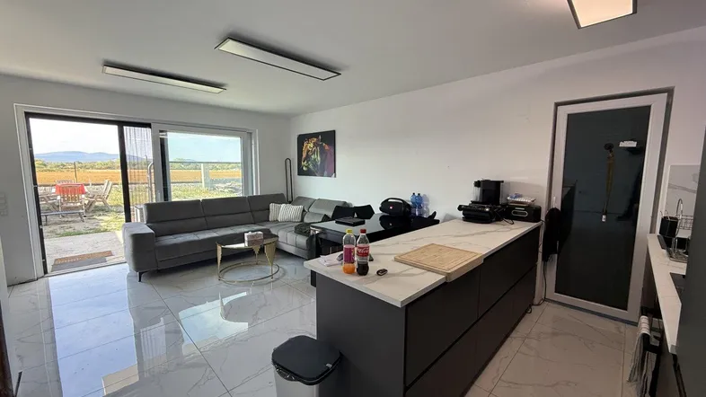 Moderner offener Wohnbereich mit integrierter Küche, großem Sofa und Zugang zur Terrasse mit Weitblick.