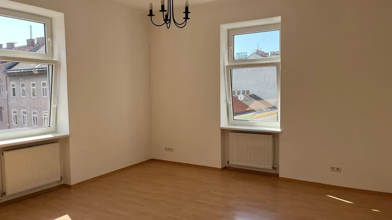 Helles Wohnzimmer mit Laminatboden, weißen Wänden und Blick auf die Stadt.