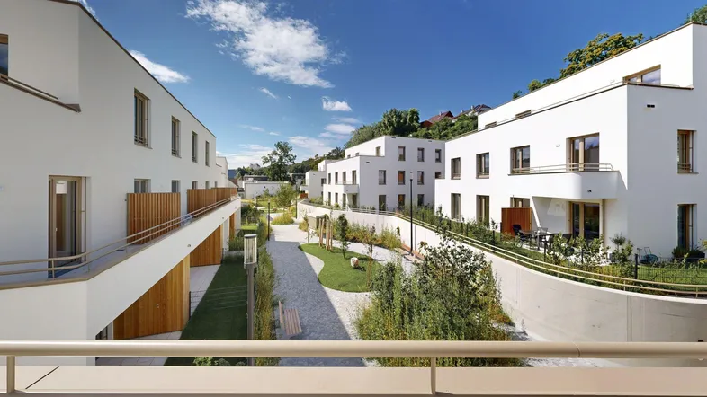 Moderne Wohnanlage mit weißen Fassaden, Balkonen und gepflegten Grünflächen unter blauem Himmel.