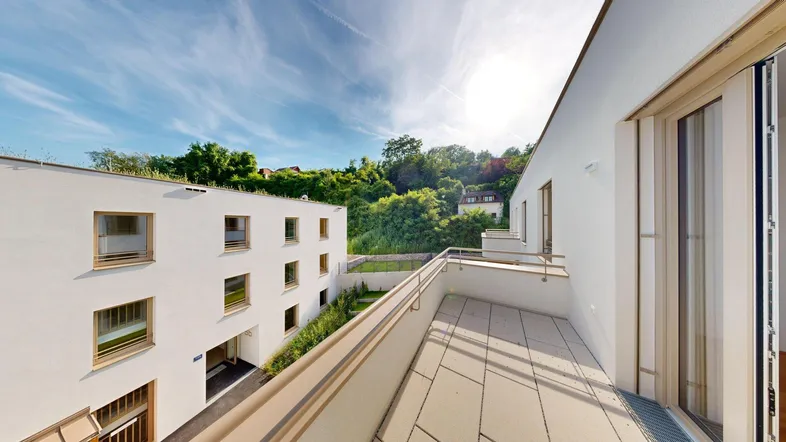Großer Balkon mit Fliesenboden und Blick auf die umliegende grüne Landschaft und moderne Gebäude.