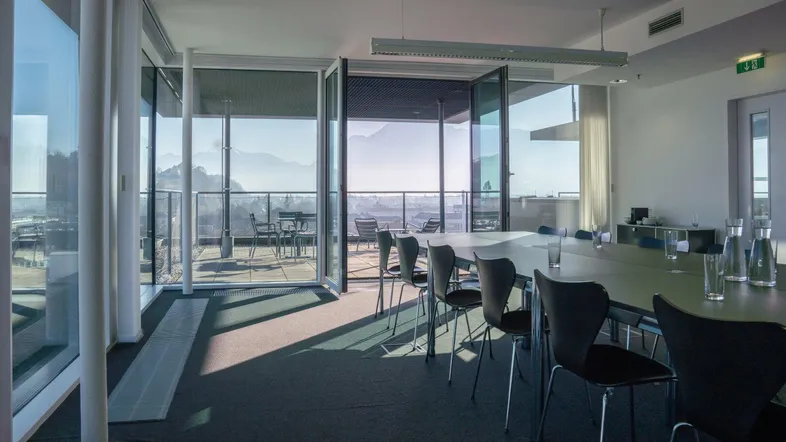 Moderner Konferenzraum mit raumhohen Fenstern, die einen weiten Blick auf die Stadt und die Berge bieten.