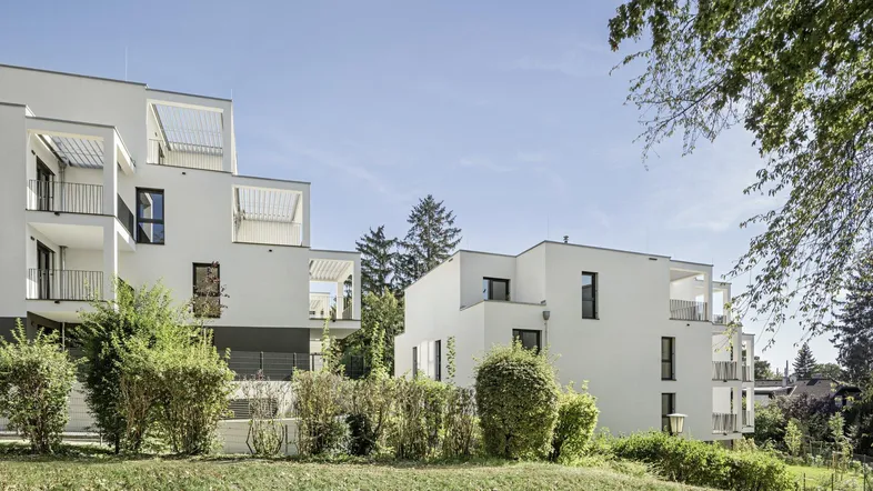 Moderne Wohngebäude mit weißer Fassade, Balkonen und umgebender Grünfläche.