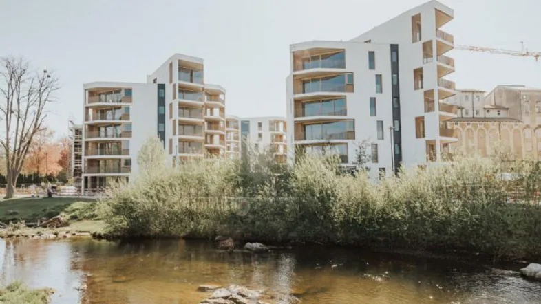 Moderne Wohngebäude mit Balkonen am Flussufer unter hellem Himmel.