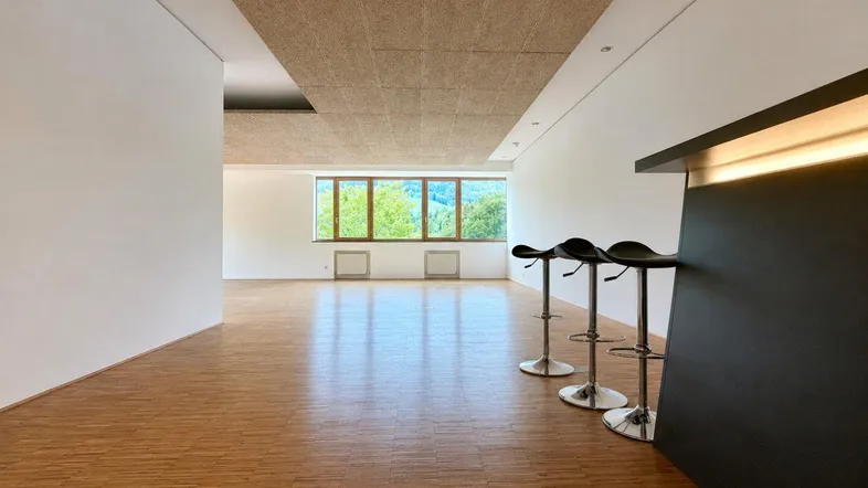 Geräumiger, leerer Gewerberaum mit Holzboden, großen Fenstern und einer modernen Bar.