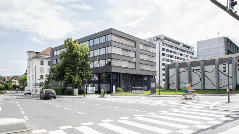 Modernes Bürogebäude an einer belebten Kreuzung mit großen Fenstern und umliegender Stadtlandschaft.