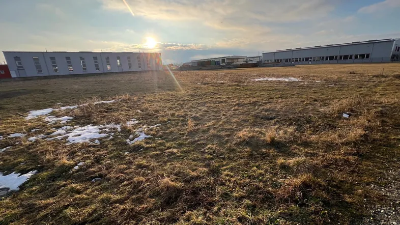 Weitläufiges unbebautes Grundstück mit Blick auf Industriegebäude unter einem sonnigen Himmel.