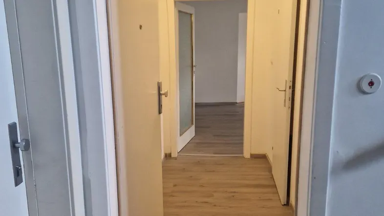 Blick durch eine offene Tür in einen hellen Flur mit Laminatboden und weiteren Türen.