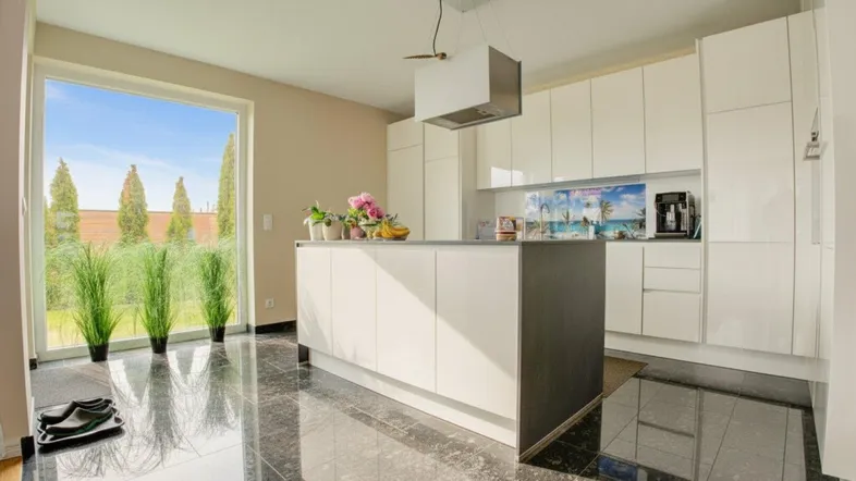 Moderne Küche mit Kochinsel, weißen Hochglanzfronten und großem Fenster zum Garten.