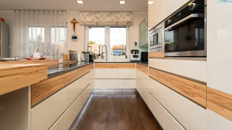 Moderne Küche mit Holzakzenten, Einbaugeräten und dunklem Boden, hell beleuchtet durch Fenster.