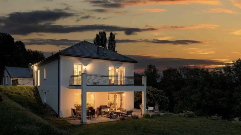 Beleuchtete Villa bei Sonnenuntergang mit gemütlicher Terrasse und weitem Blick in die Natur.