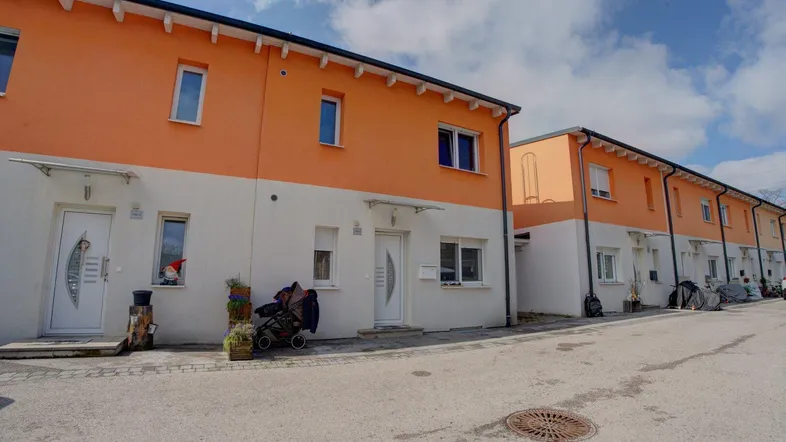 Reihenhäuser mit orange-weißer Fassade und Satteldach in einer Wohnsiedlung.