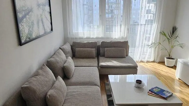 Helles Wohnzimmer mit großem Ecksofa, Holzboden und Blick auf die Stadt.