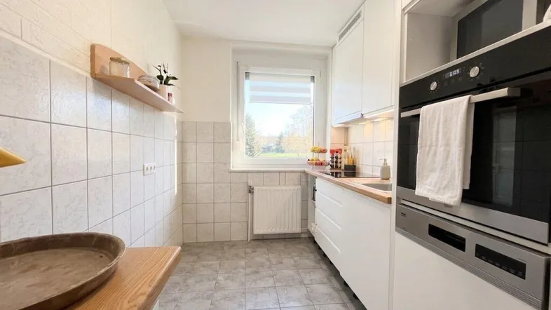 Funktionale Küche mit weißen Schränken, Holz-Arbeitsplatten und integriertem Backofen, hell und sauber.