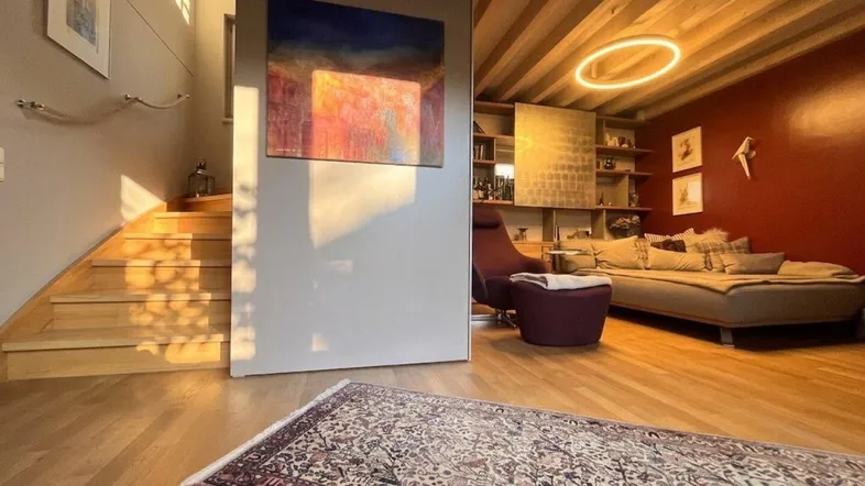 Helles Wohnzimmer mit Holzbalkendecke, Parkettboden und Zugang zur Treppe.