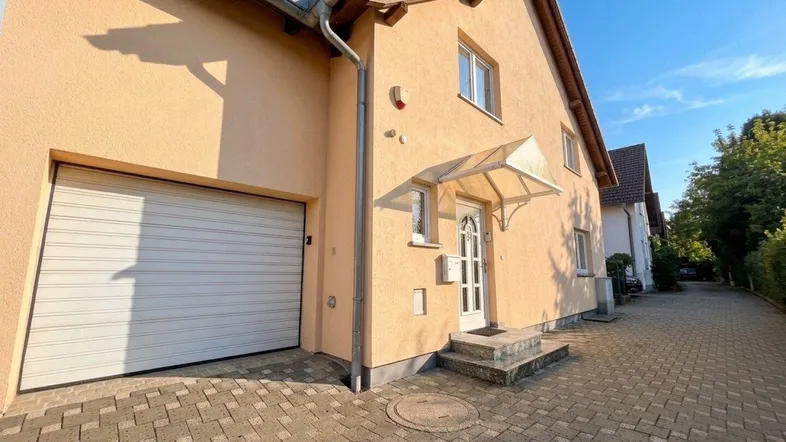Vorderansicht des Hauses mit Garagentor und gepflastertem Zugangsbereich unter blauem Himmel.