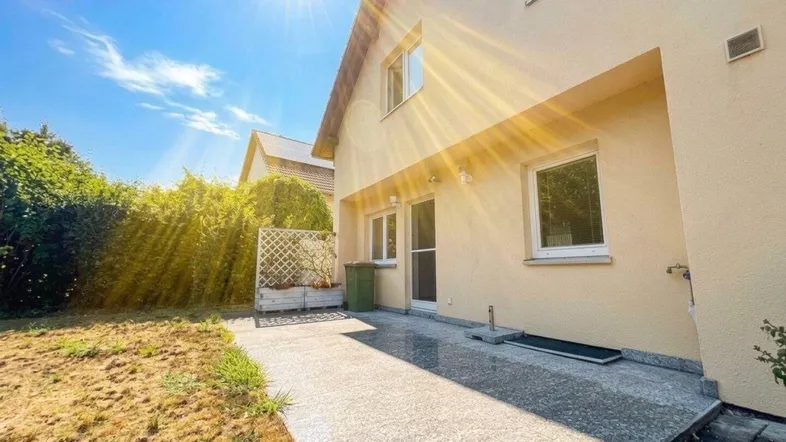 Sonnige Terrasse mit gepflastertem Bereich und angrenzendem Rasen im Garten.