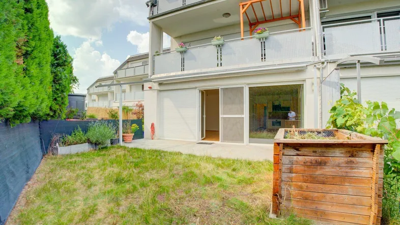 Außenansicht des Gebäudes mit Terrasse, kleinem Gartenbereich und Balkonen im Obergeschoss.