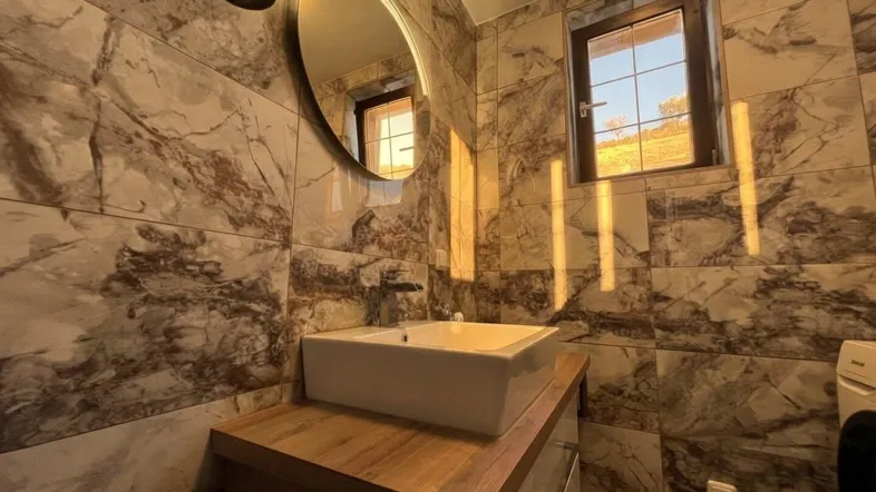 Modernes Badezimmer mit Marmoroptik-Fliesen, Aufsatzwaschbecken und beleuchtetem Spiegel.