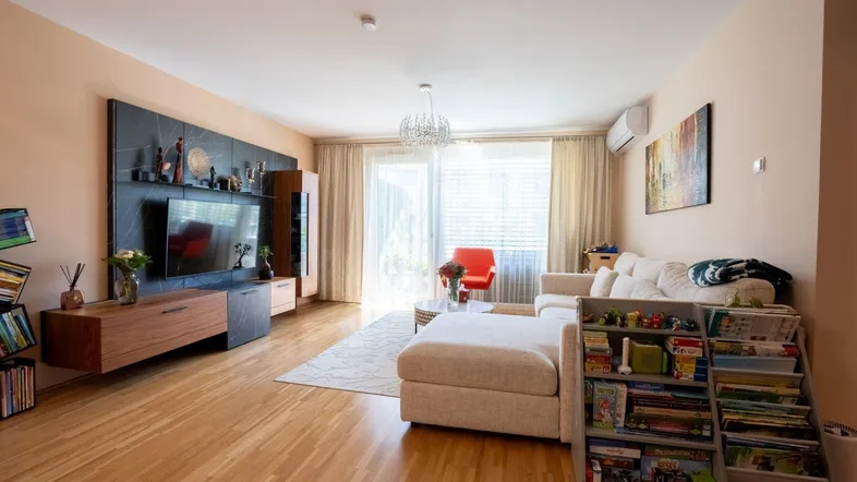 Helles Wohnzimmer mit Parkettboden, beiger Couch und modernem TV-Möbel. Klimaanlage ist sichtbar.
