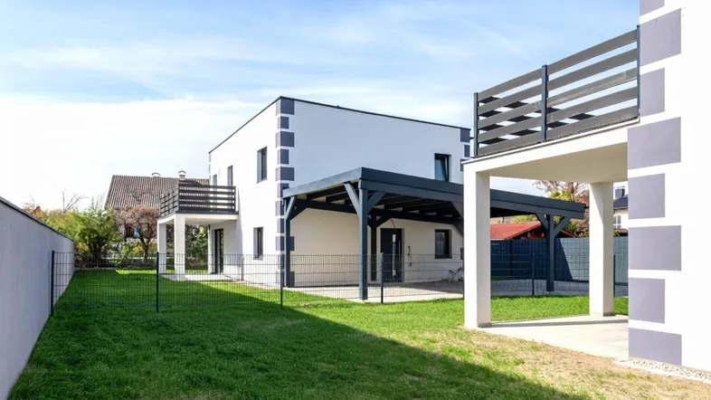 Außenansicht eines modernen Hauses mit Garten, Rasenfläche und überdachter Terrasse.