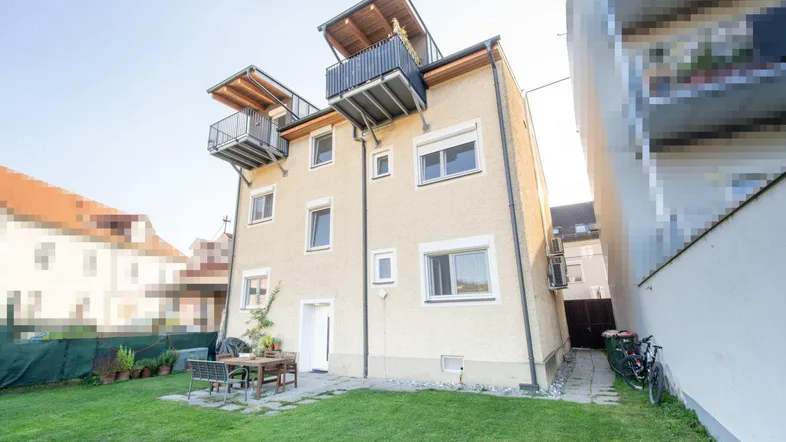 Hinteransicht des Hauses mit Garten, Terrasse und mehreren Balkonen, ideal für Entspannung im Freien.