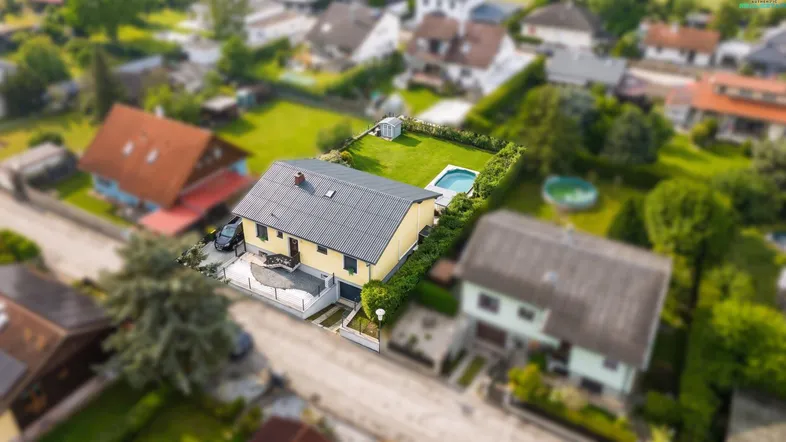 Luftaufnahme des Hauses mit Garten, Pool und umliegender Wohnsiedlung, eingebettet in eine grüne Umgebung.