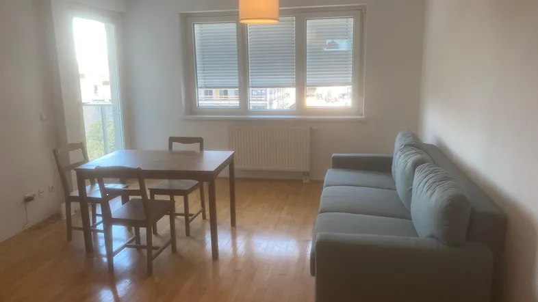 Helles Wohn- und Esszimmer mit Parkettboden, Sofa und Esstisch, sowie Zugang zum Balkon.
