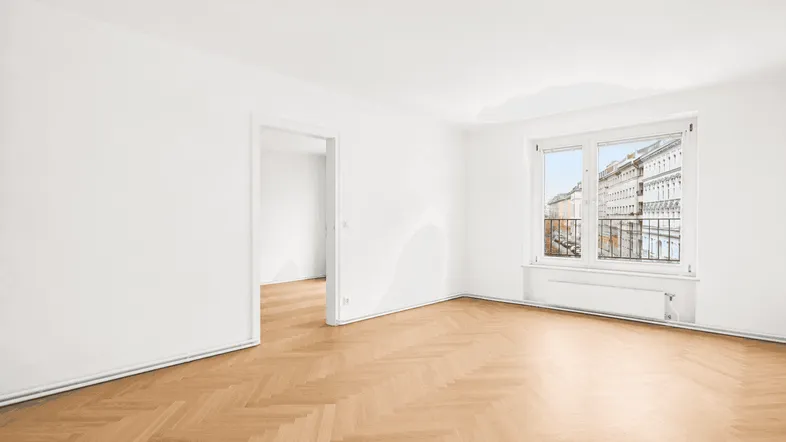 Helles Zimmer mit Fischgrätparkett und Blick auf die Stadt, ideal als Wohn- oder Schlafzimmer.