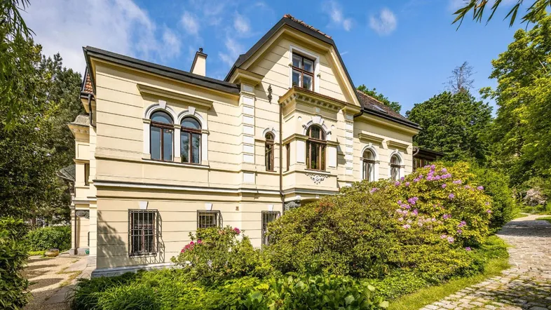 Eine elegante Villa mit klassischer Architektur, umgeben von üppigem Grün und Bäumen unter blauem Himmel.