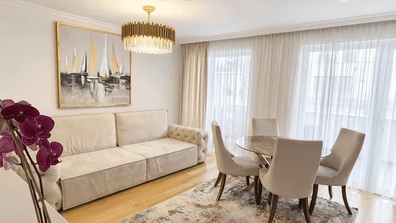 Heller Wohn- und Essbereich mit beigem Sofa, modernem Kronleuchter und Zugang zum Balkon.